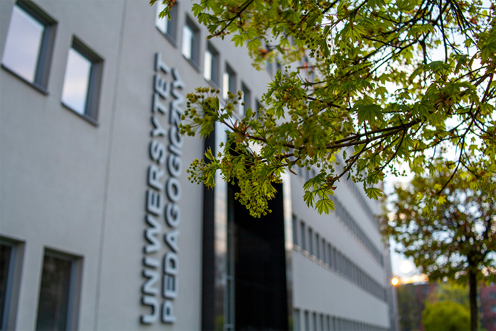 fasada budynku głównego Uniwersytetu Pedagogicznego w Krakowie od ul. Warmijskiej; na pierwszym planie kwitnące drzewo