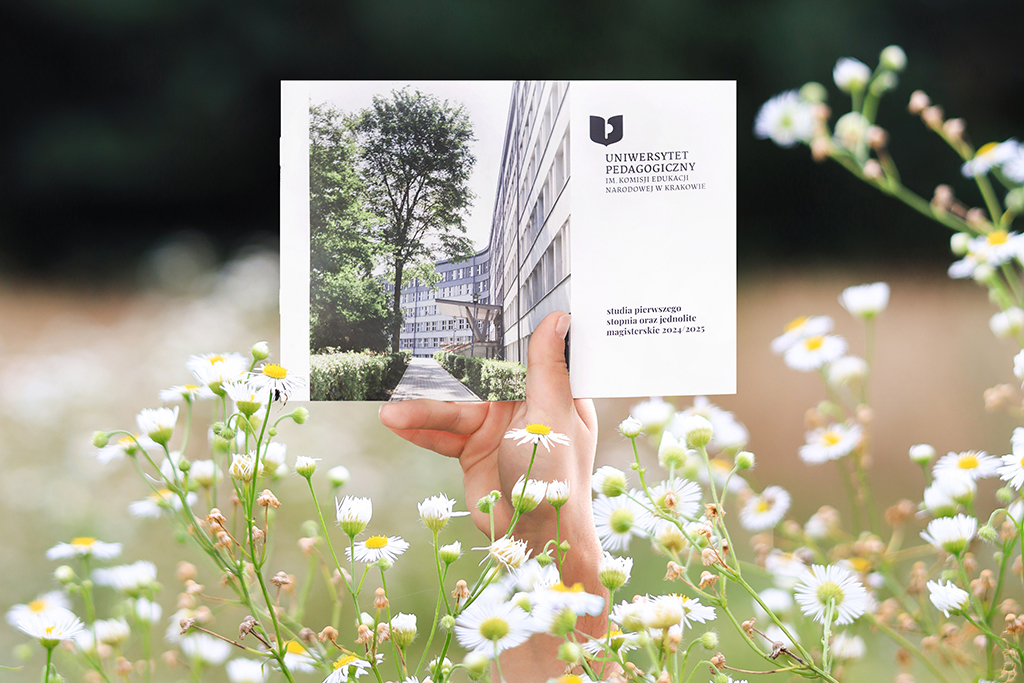 dłoń trzymająca Informator dla kandydatów na studia pierwszego stopnia i jednolite magisterskie 2024/2025, na pierwszym planie białe kwiaty 