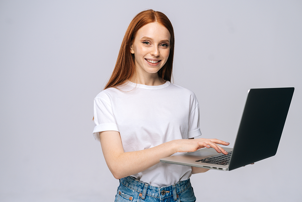 rudowłosa uśmiechnięta dziewczyna trzymająca w rękach laptopa