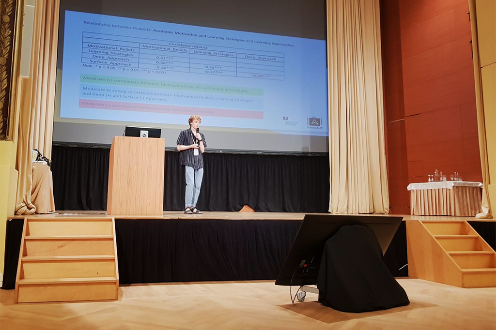 Konrad Guzowski prowadzący odczyt na jednej z konferencji naukowych, w tle ekran z prezentacją